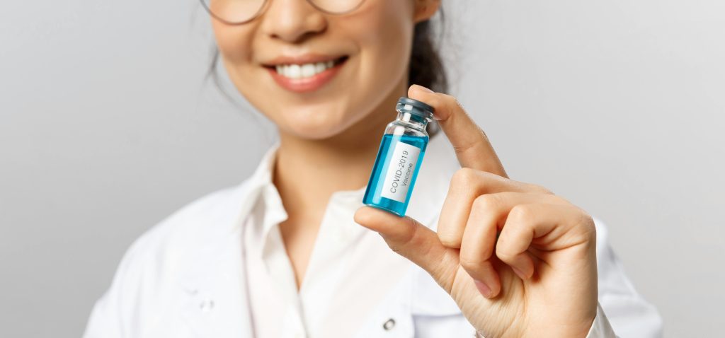 A close-up of a smiling doctor holding a COVID-19 vaccine vial.